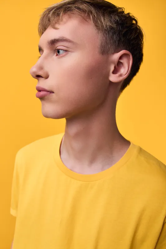 Young man profile in yellow shirt against a colorful background, studio lighting and clean composition emphasize fashion, youth and modern stock imagery for advertising and editorial use