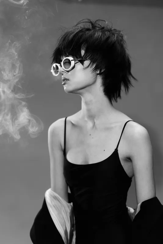 Black and white portrait of a stylish woman wearing sunglasses with a short hairstyle and smoke background.