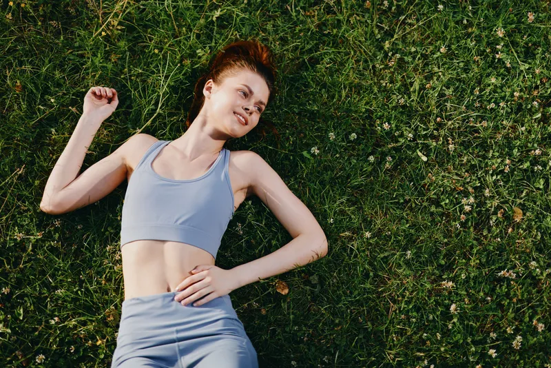 Young woman in athletic wear relaxing on grass, showcasing outdoor fitness and well being with a serene expression Perfect for health and wellness concepts