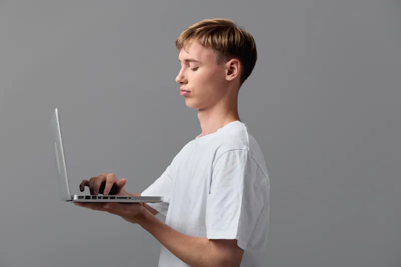 Man in a white t shirt typing on a slim laptop, side view, focused on the screen, studio backdrop, modern digital work setup, remote work scene in a clean minimalist space