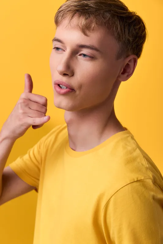 Man with a thumbs up wearing a yellow shirt, cheerful casual gesture conveying positive mood and confident vibe against a bright studio backdrop