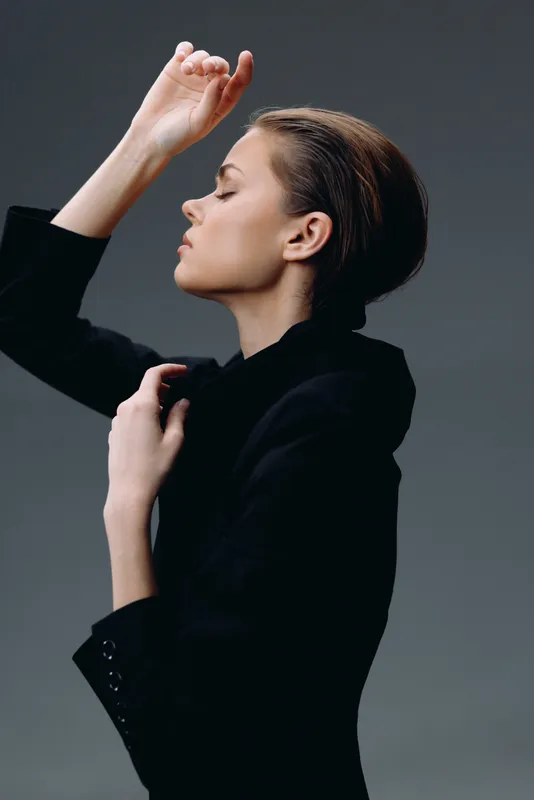 Profile of a woman in a black blazer with eyes closed and graceful pose on dark background