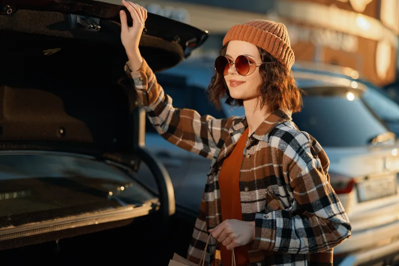 woman car trunk shopping sunglasses beanie plaid sunlight authentic candid lifestyle portrait of a young shopper at golden hour glow, mindful living vibe and emotional storytelling in urban style