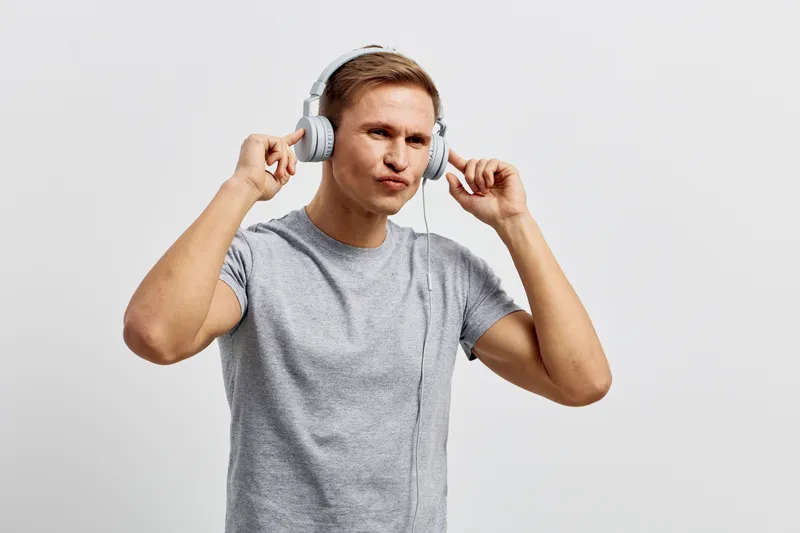 Young man wearing casual gray t-shirt listening to music through large headphones against plain white background, relaxed and focused, studio shot, lifestyle concept, modern technology.