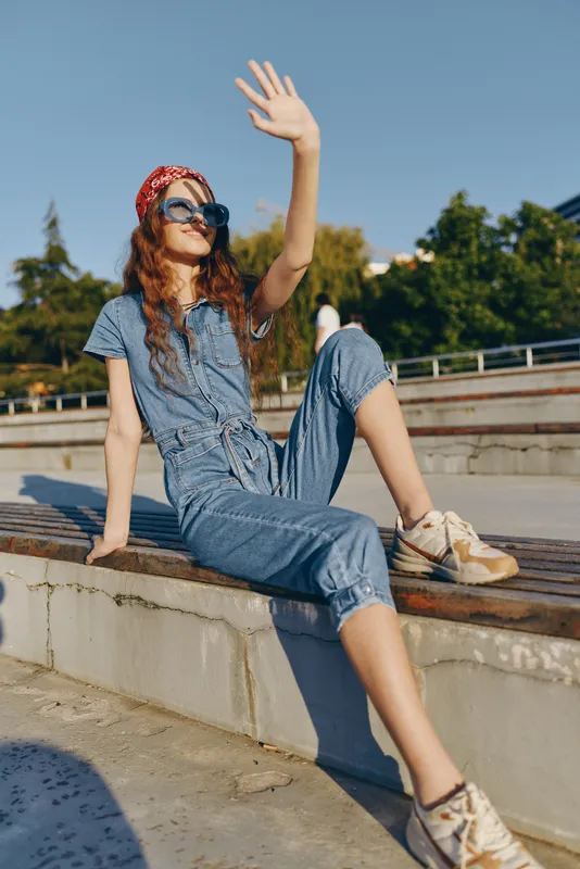Lifestyle woman in modern boho-western denim street style wearing sunglasses and a red bandana, relaxing outdoors with film color warmth and casual summer vibe.