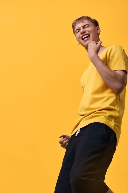 Joyful motion, energetic pose, yellow shirt, orange backdrop, cheerful vibe, dynamic expression capture a lively moment of casual fashion and self confidence in a studio setting, highlighting color,
