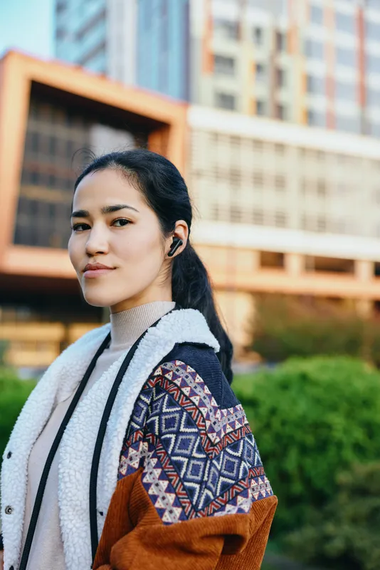 Outdoor street style featuring a confident woman in a patterned shawl and cozy coat against a modern city backdrop, urban scenery and fashion focus, candid lifestyle moment with daylight and texture