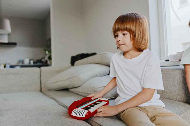 Playful boy with a red keyboard, enjoying music in a cozy living room setting, expressing creativity and joy through play.