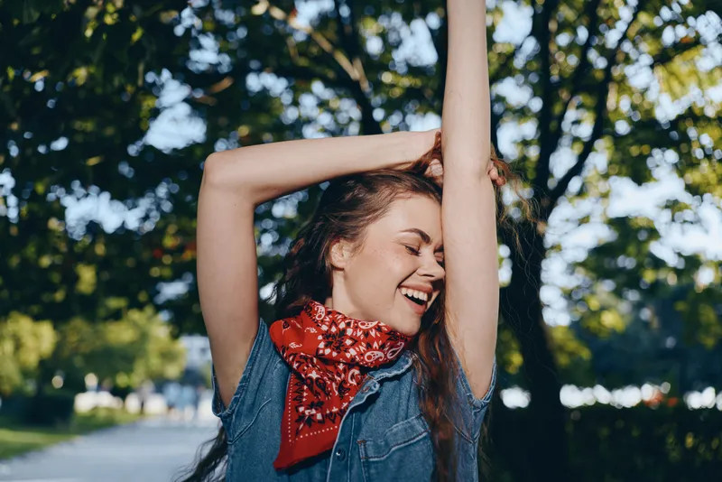 Lifestyle woman wearing modern boho-western denim street style with a red bandana, enjoying the outdoors with a bright film color aesthetic and natural sunlight.