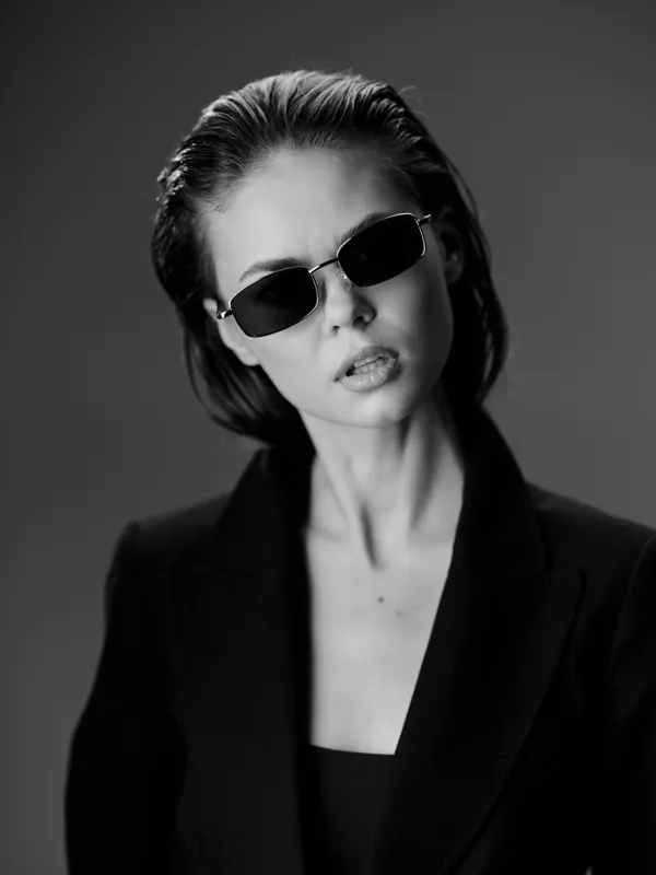Black and white portrait of a stylish woman wearing sunglasses and a suit with a confident expression.