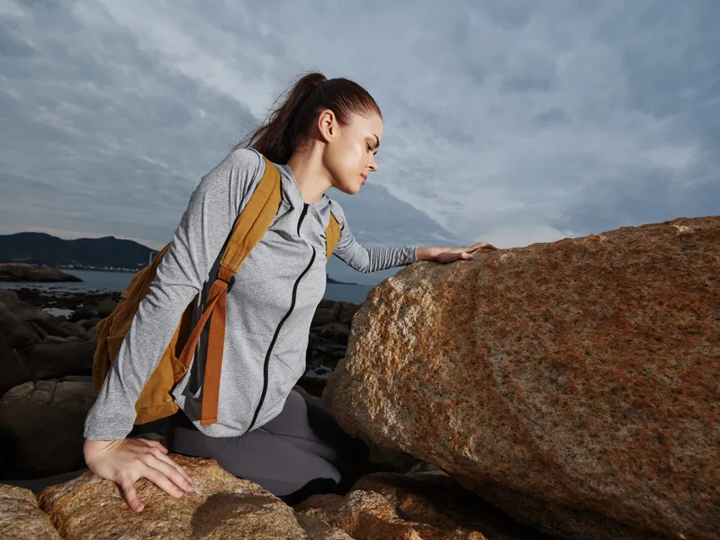A young woman of mixed heritage exploring rocky shores, dressed in athletic gear, showcasing determination and adventure against a moody coastal backdrop