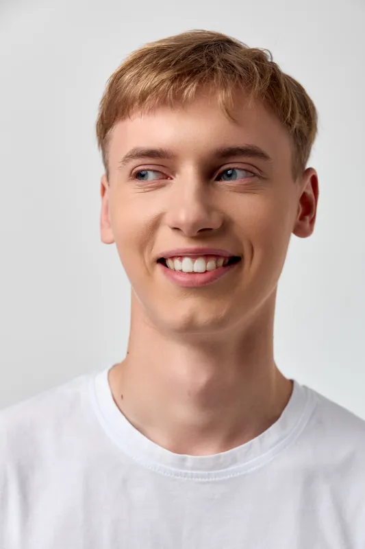Smiling man wearing a white t shirt, casual and friendly, looking slightly to the side with a bright natural vibe suitable for lifestyle, wellness and positive energy imagery