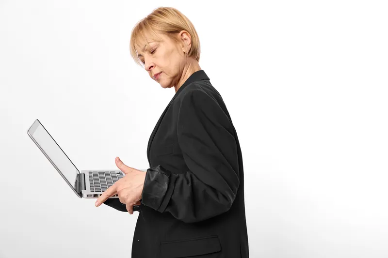 woman laptop typing office technology business communication remote work stress, adult female in black suit indoors, typing on portable computer, focused profile, white background