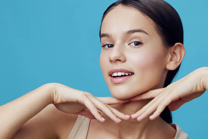 Young woman with a joyful expression showcasing clear skin against a pastel blue background, embodying beauty and confidence in a trendy look