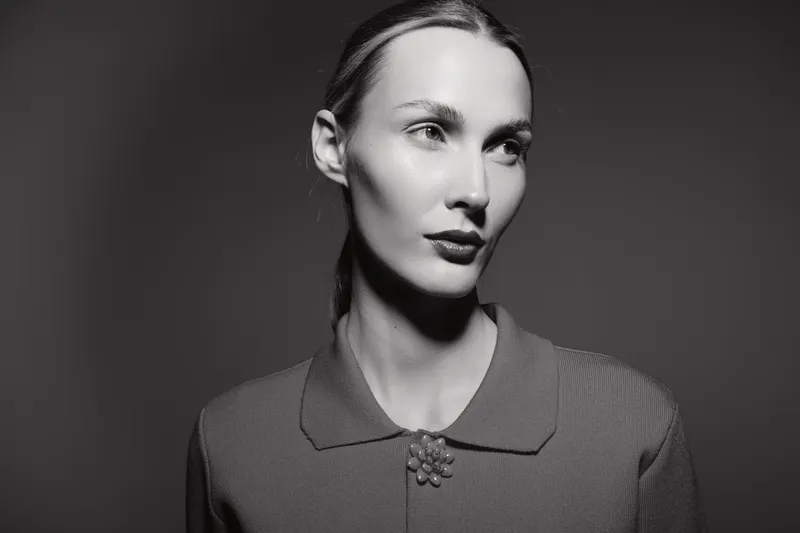 Portrait of a young Caucasian woman with pale skin and slicked-back hair wearing a vintage sweater with a brooch. Concept of retro style and classic beauty in monochrome.