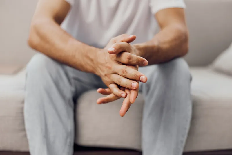 Thoughtful man sitting on a sofa, hands clasped, showcasing a relaxed and contemplative mood. Ideal for themes of introspection and relaxation in modern life.