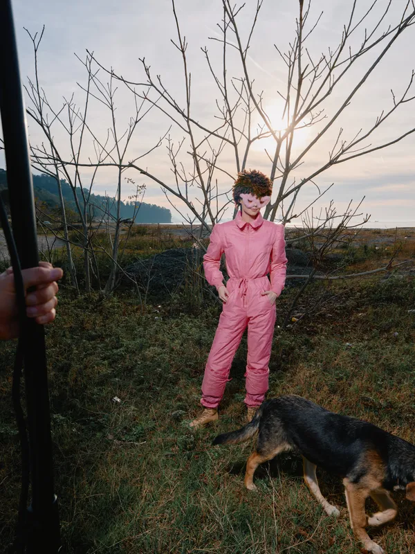 Person in pink jumpsuit outdoors with a dog on a grassy field during sunset, trees silhouette and calm atmosphere, natural lighting, simple composition for lifestyle or fashion stock