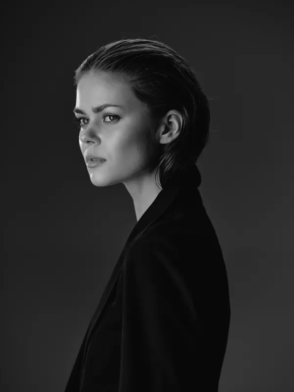 Black and white portrait of a serious woman with slicked-back hair wearing a dark jacket on gray background