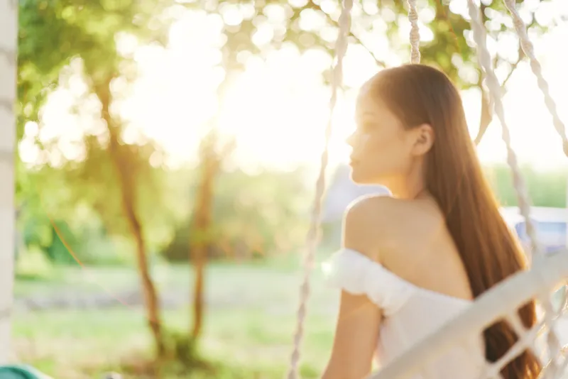 A serene young woman in a summer dress, reflecting on life in a sunlit garden, embodying tranquility and beauty in nature