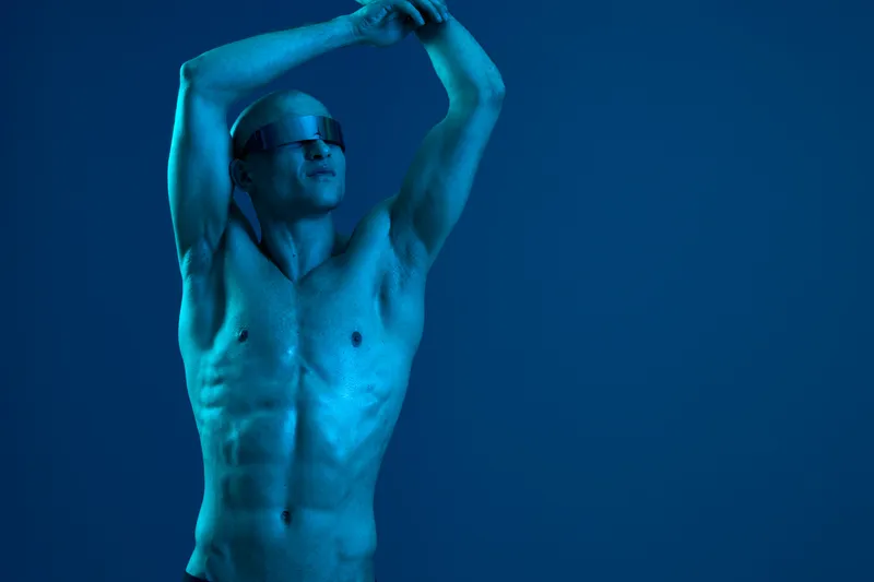 Athletic man with sunglasses poses confidently against a blue background, showcasing strength and style. The image captures a vibrant energy and modern appeal.