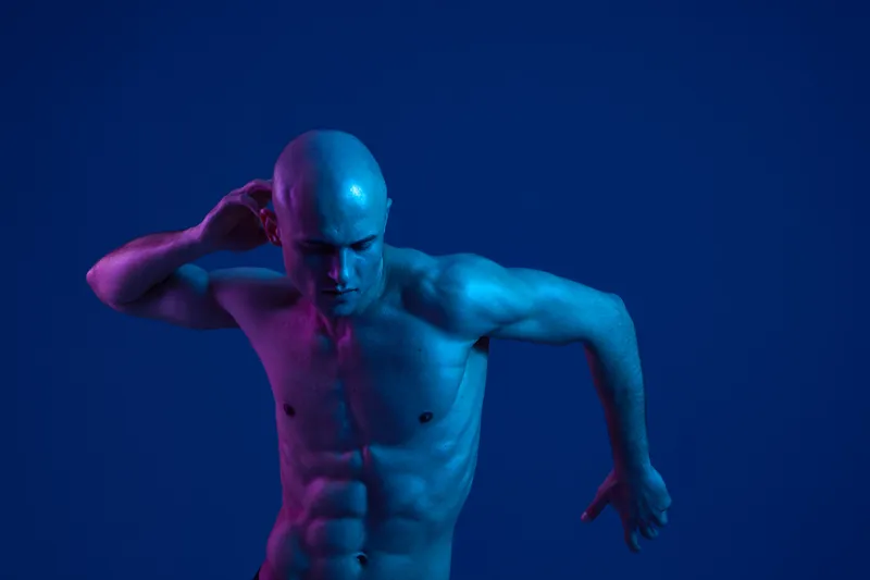 Athletic man posing in dynamic blue lighting, showcasing a strong physique. The composition emphasizes motion and intensity, creating a captivating visual impact.