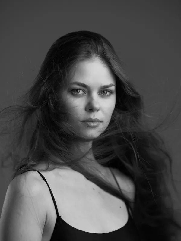 Black and white portrait of a young woman with flowing hair, natural expression, and minimalist style captured on a dark background.