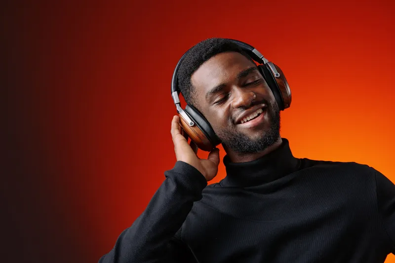 Young African man enjoying music with headphones against a vibrant orange background, expressing joy and relaxation through his smile
