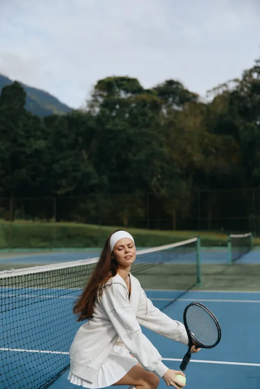 Young woman enjoying tennis on a sunny day, dressed in a white sports outfit, smiling with confidence on the blue tennis court background