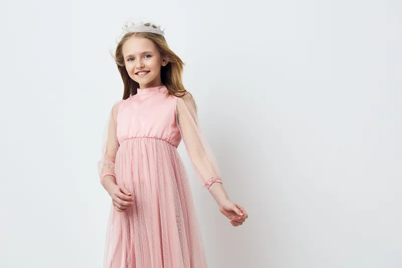 Young girl in a pink dress, smiling with a crown, representing joy and innocence, on a white background, perfect for children s fashion and celebrations