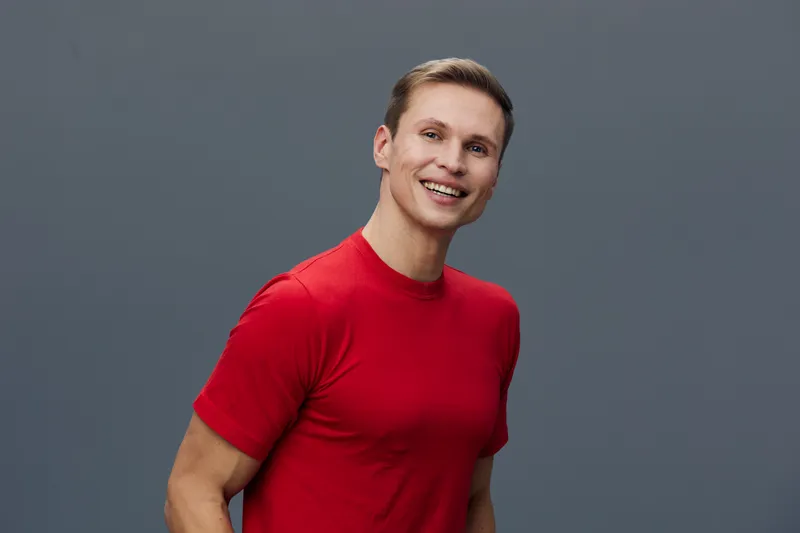 Smiling young man wear red t-shirt look camera isolated on gray background studio portrait cheerful positive emotion lifestyle concept