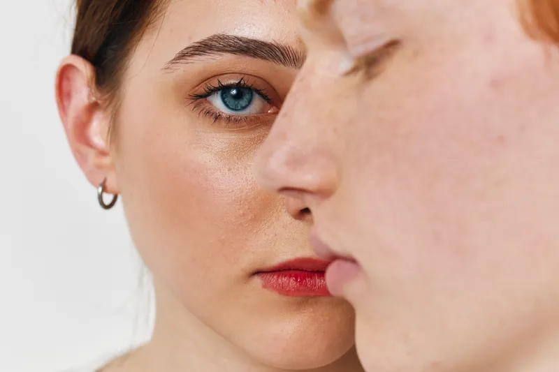 Closeup of two young women faces with clear skin and natural makeup in studio. Focus on blue eyes, freckles and earrings on female model in selective sharpness portrait.