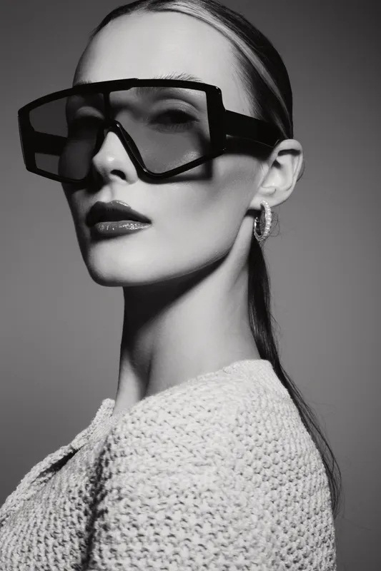Stylish fair-skinned Caucasian woman wearing large futuristic glasses and knitted sweater in black and white studio portrait. Concept of fashion and modern eyewear.