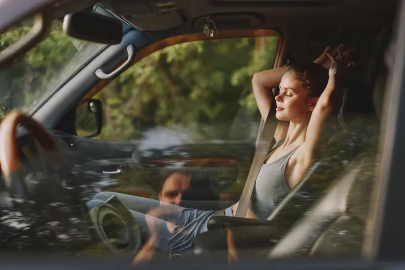Calm young woman enjoying a moment of relaxation in her car, wearing casual sportswear, with a serene expression and a lush green background