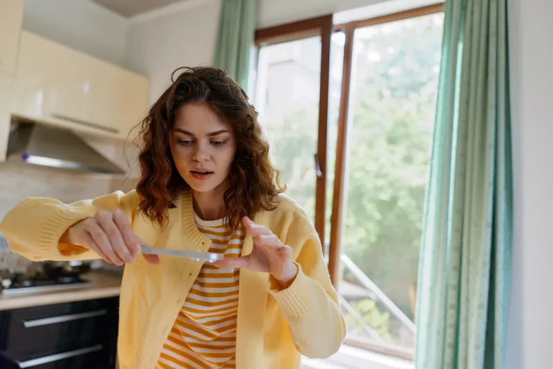 A stressed woman in a yellow cardigan examines a ruler in a bright kitchen, capturing a moment of home care and daily challenge in a busy lifestyle, expressing focus and resilience in domestic life.