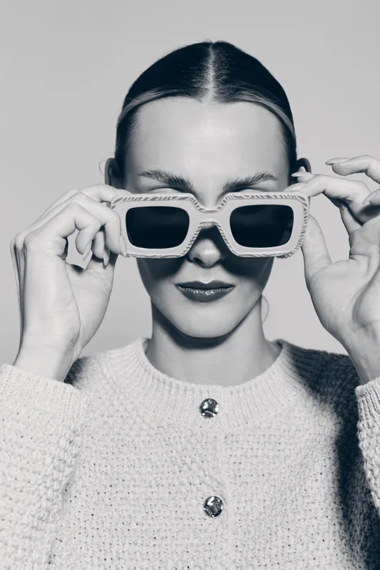 Portrait of a young white woman with pale skin wearing knitted sweater and stylish sunglasses in black and white. Concept of fashion, elegance, and modern accessories.