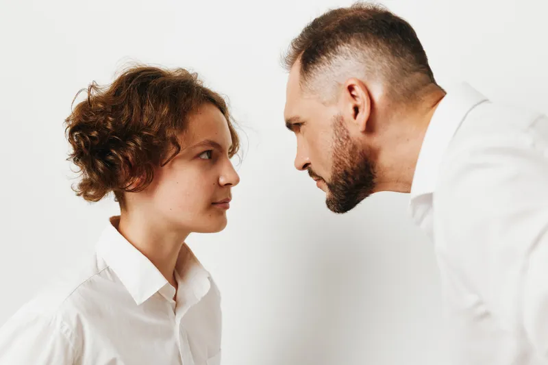 A professional business man faces a colleague with focused emotion, their posture and gaze set against an isolated colored background, signaling tension, trust, and collaboration.