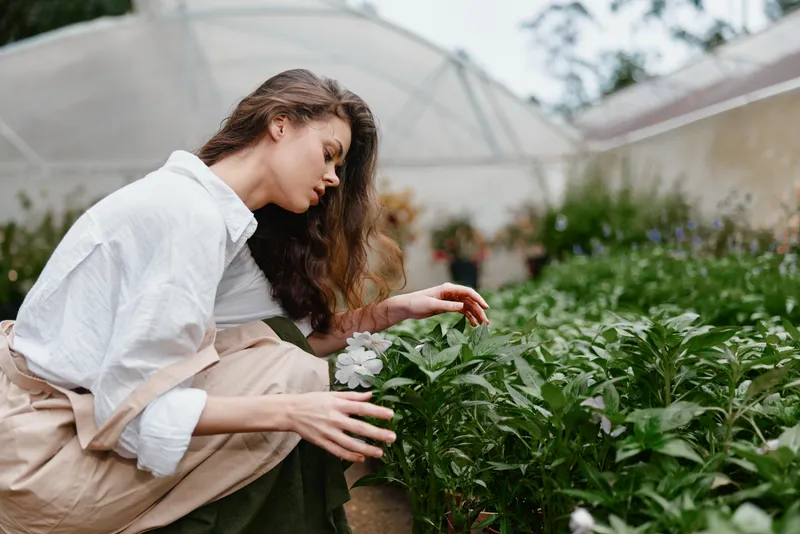 Young woman in white shirt and beige skirt tending to plants in a greenhouse, showcasing a passion for gardening, serenity, and a connection with nature