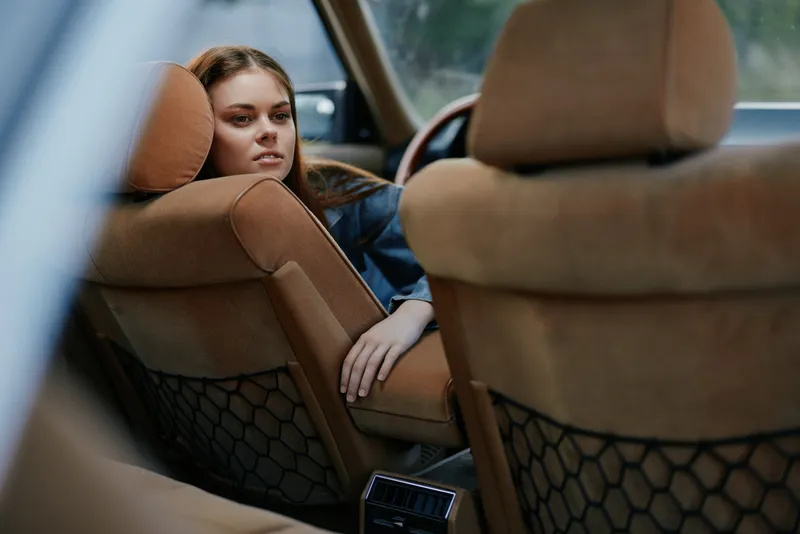 Thoughtful young woman in a car interior, showcasing emotions of contemplation and introspection against a soft, neutral background.