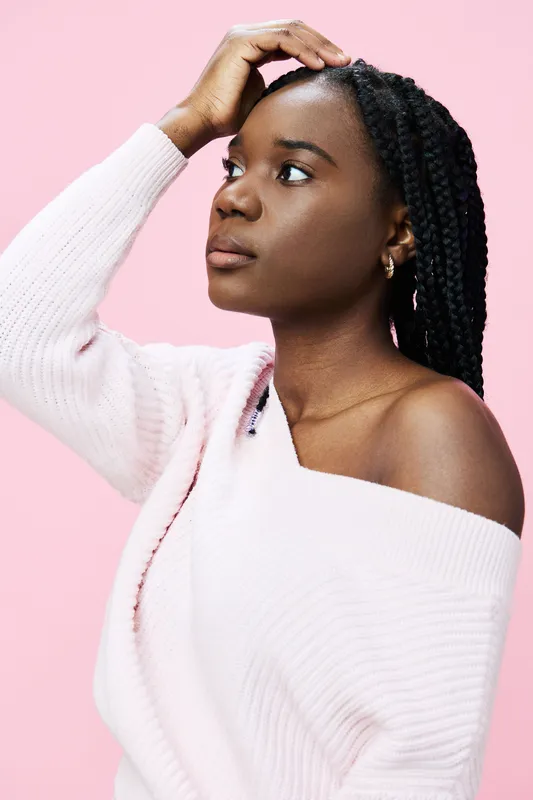 Thoughtful young woman with braided hair in soft pink sweater against a pastel pink background, representing self reflection and calm emotions