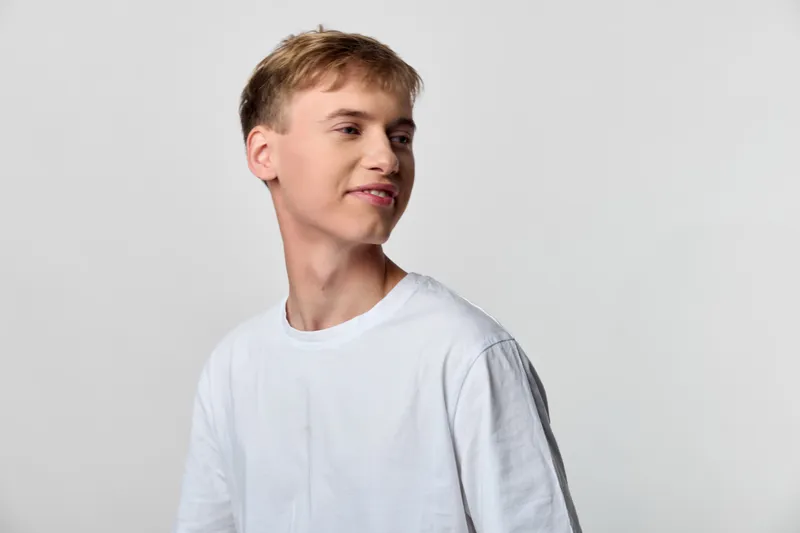Young man wearing a white tshirt with a relaxed smile, looking to the side in a clean studio setting, casual mood, natural lighting, simple fashion shot without branding or accessories.