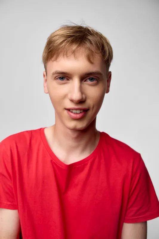 Close up of a smiling young man in a red t shirt, studio lighting, clean background, confident expression, casual style, focused on facial features and mood, suitable for stock use and editorial