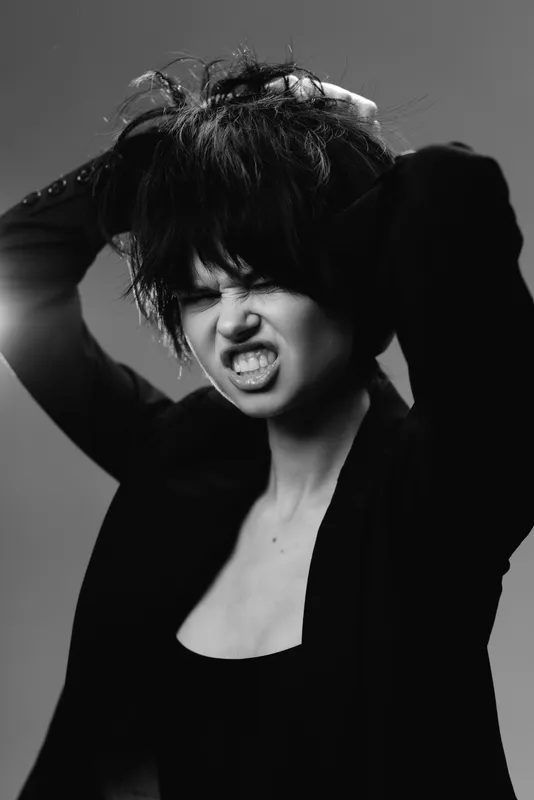 Angry woman with messy hair in black and white expresses frustration with intense emotion and dark background.