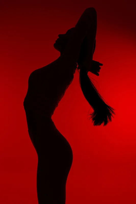 Silhouette of a woman sport fitness stretching against a red background, highlighting her athletic posture and toned figure in dynamic motion.