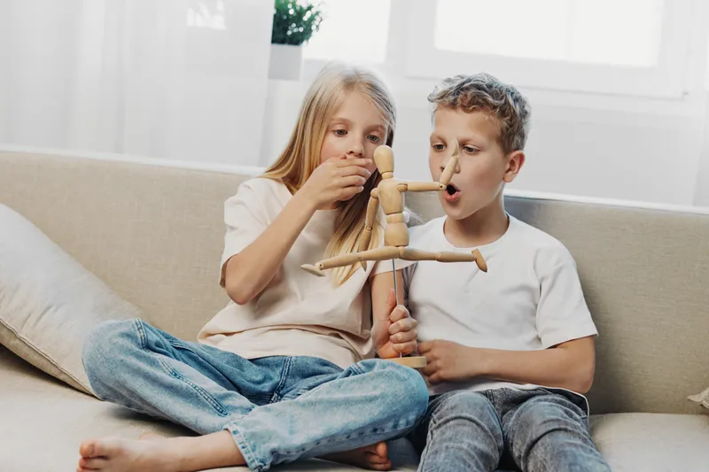 Two children sitting on sofa playing with wooden mannequin, focused on creativity and imagination in bright cozy living room setting.