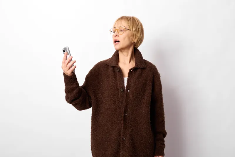 Stressed blonde woman holds an electronic cigarette, vaping on a plain white background, mouth open as if tired, isolated studio concept for nicotine stress and health