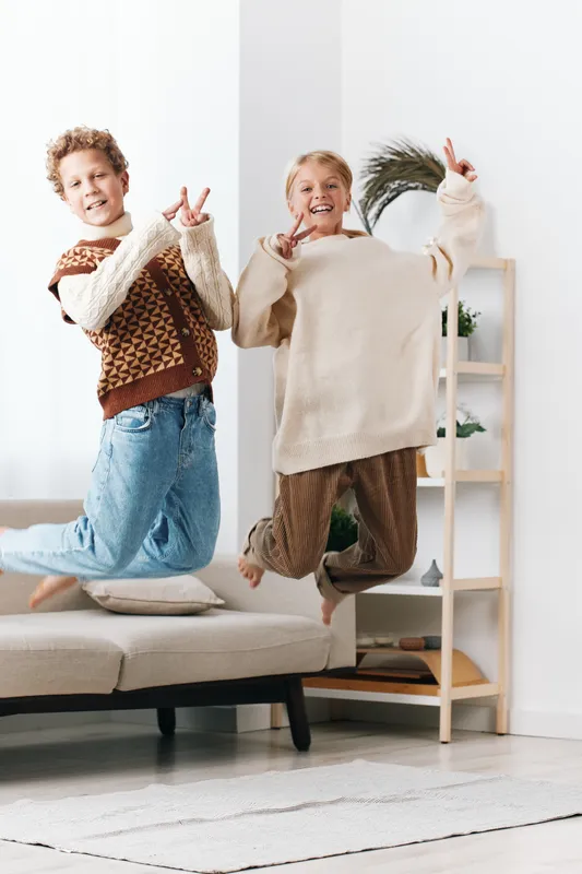 Authentic playful moment of children at home, capturing a school ready lifestyle as they jump and pose with joy, showcasing energy, warmth, and genuine smiles.