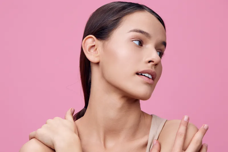 Portrait of a young Hispanic woman with minimal makeup, showcasing natural beauty against a soft pink background, conveying confidence and serenity