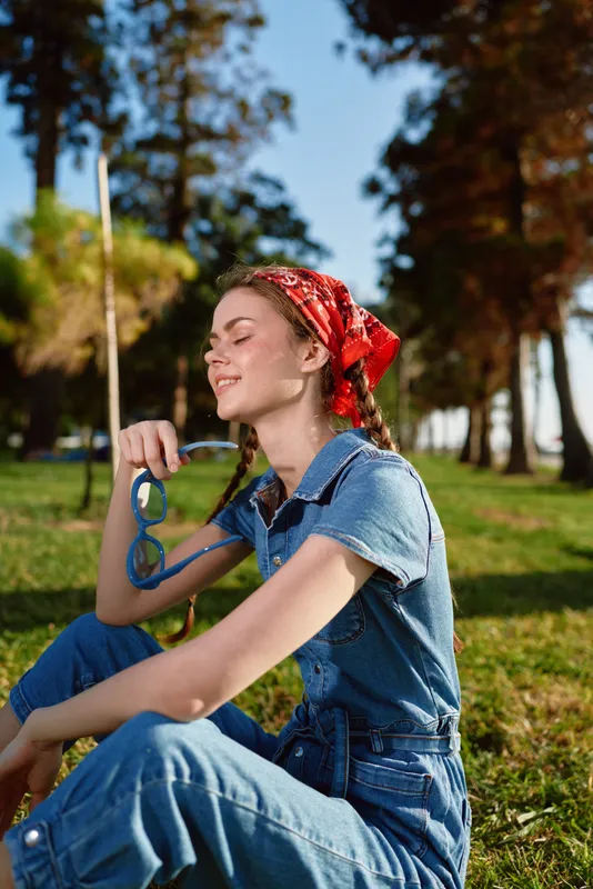 lifestyle woman relaxing outdoors in denim outfit with red bandana and sunglasses, modern boho-western denim street style, film color, peaceful sunny day in nature