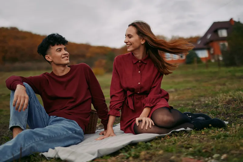 A genuine candid portrait of a young couple sitting on a picnic blanket in a rural field, sharing an authentic moment of connection and relaxed companionship.