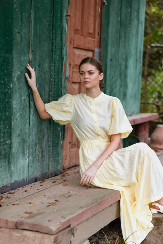 Woman dress yellow outdoor portrait fashion pose calm natural light on a relaxed subject beside a weathered doorway, creating a refined image with warmth and thoughtful, peaceful mood.